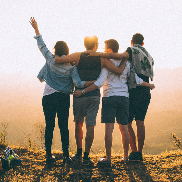 Four people stand on a hill, embracing each other with their arms around one another